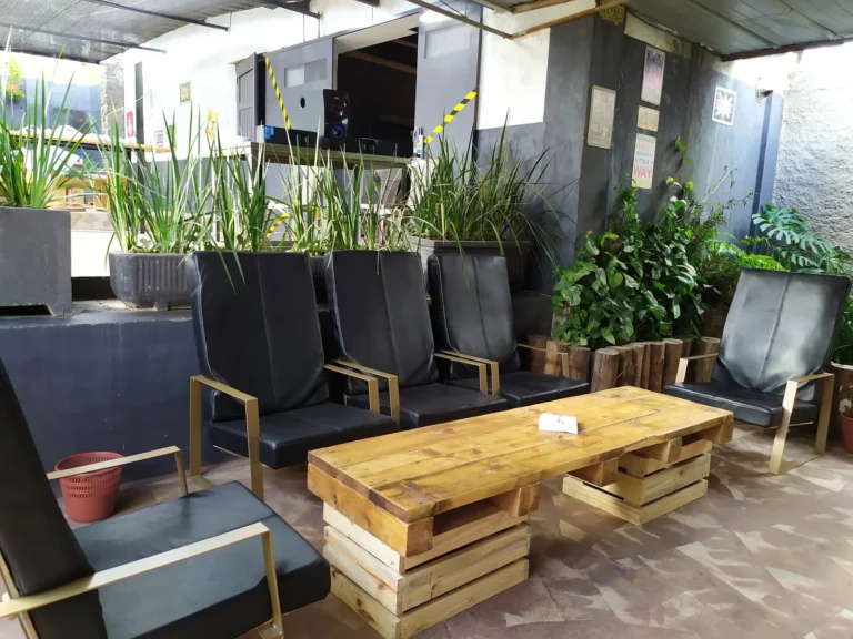 Salon extérieur : fauteuils noirs et table en palettes entourés de plantes